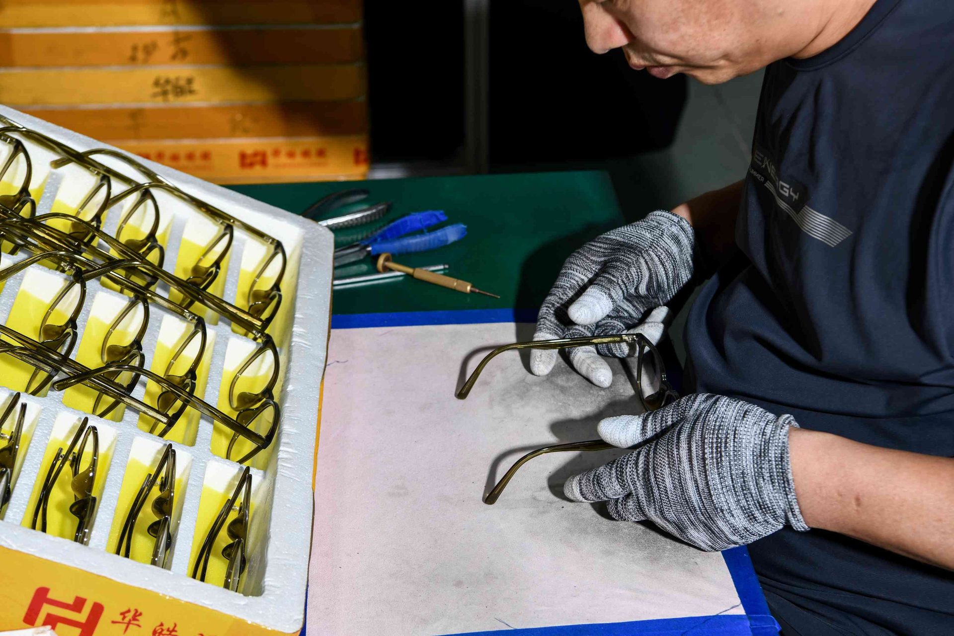 Close-up of a gloved worker inspecting a metal eyewear frame during assembly at HAO Eyewear