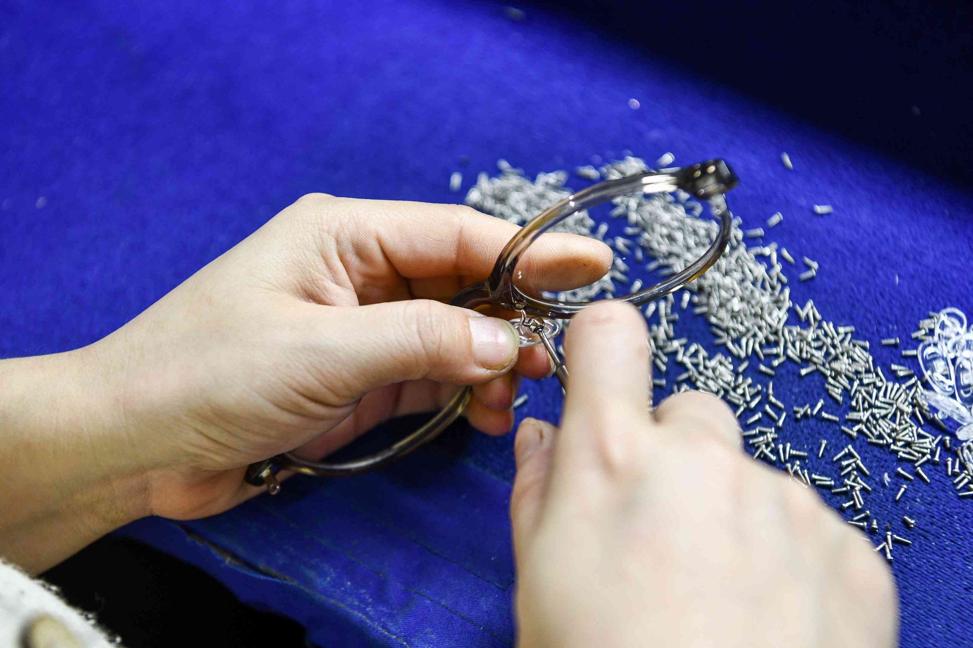 Worker fitting micro hinge screws onto a metal eyeglass frame at HAO Eyewear